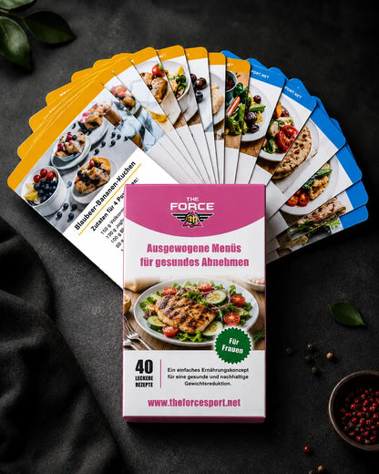 A boxed card deck titled "THE FORCE" with the German text "Ausgewogene Menüis für gesundes Abnehmen" is displayed in front of a fanned-out set of recipe cards on a dark textured surface. The box is pink and white with a salad photo, and the cards show colorful food and recipe imagery.